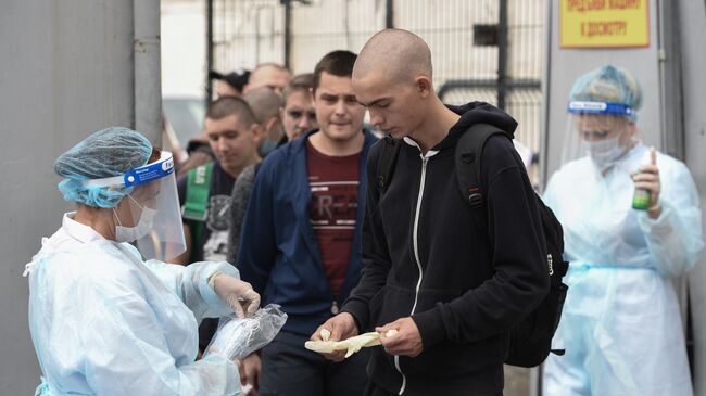 Сотрудники медслужбы раздают защитные маски и перчатки призывникам на входе в сборный пункт военного комиссариата Севастополя