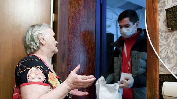 Волонтер передает доставленные на дом продукты пенсионерке