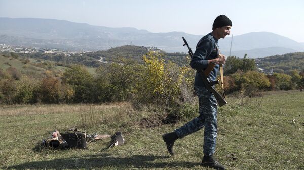 Мужчина с автоматом возле сбитого беспилотника в Степанакерте