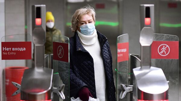 Женщина в медицинской маске проходит через турникет, с установленным дистанционным тепловизором, на станции метро Марьино 