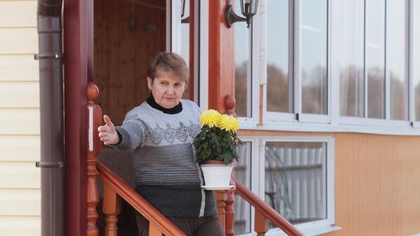 Женщина пенсионного возраста на крыльце своего дома с цветком в руке