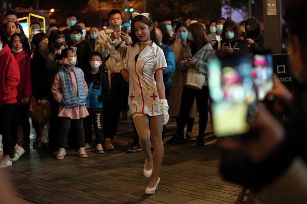 Девушка в костюме медсестры выступает перед толпой в ночь Хэллоуина в торговом районе Пекина