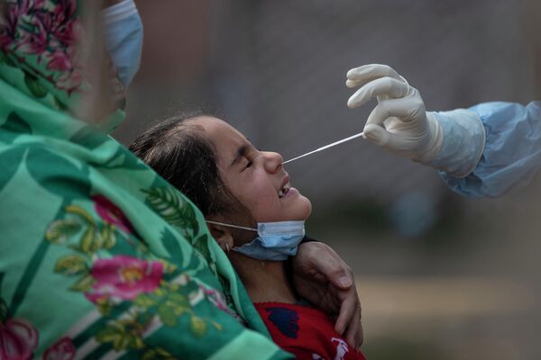 Медицинский работник берет мазок из носа  у девочки для проверки на COVID-19 в Сринагаре, Кашмир