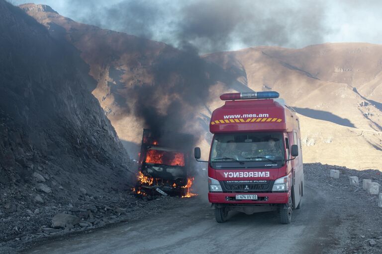 Горящий автомобиль и автомобиль скорой помощи на горной дороге в районе города Карвачар