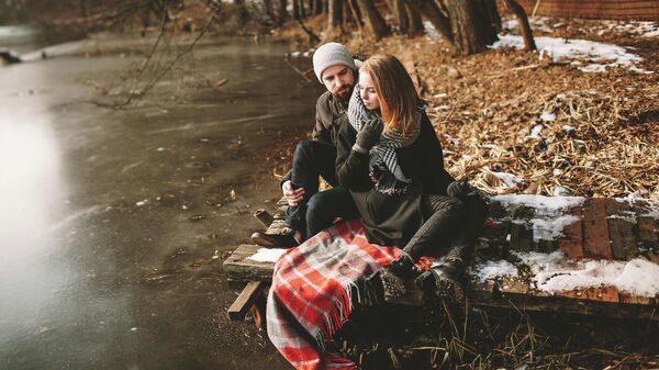 Молодая пара сидит на старом пирсе у замерзшего озера