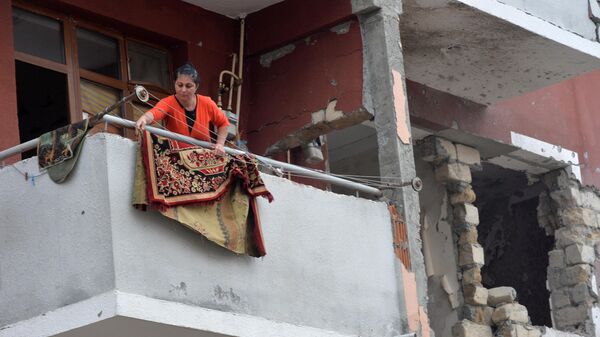 Женщина вывешивает ковер на балконе своей квартиры в доме, поврежденном в результате обстрелов в поселке Шырарх Тертерского района