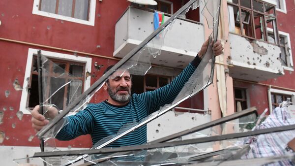Мужчина выбрасывает стекла, разбитые в результате обстрелов в поселке Шырарх Тертерского района