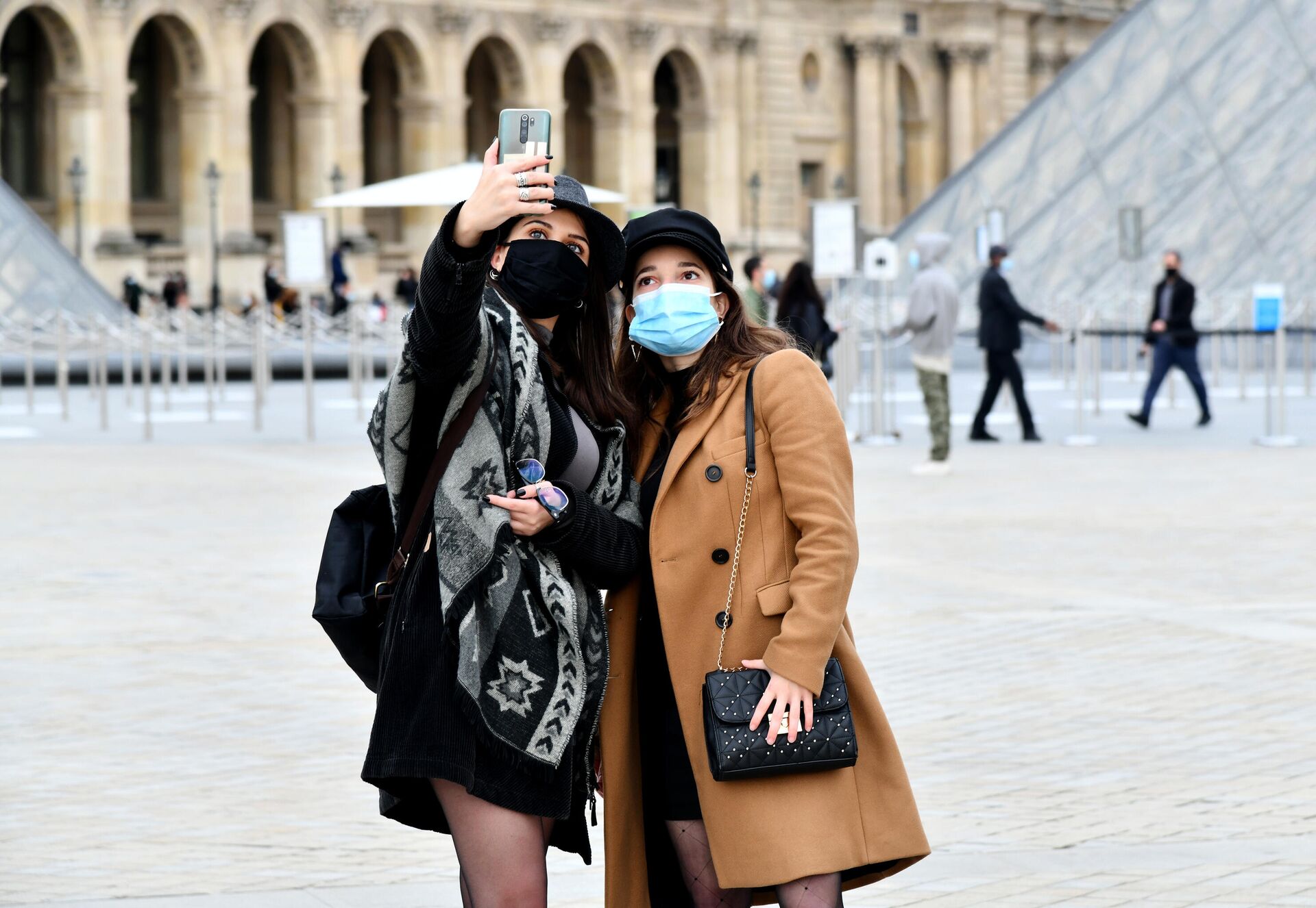 Девушки в масках фотографируются на площади у входа в музей Лувр в Париже - РИА Новости, 1920, 11.02.2022