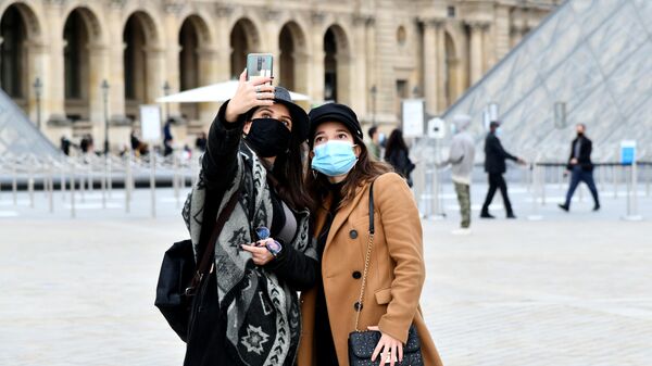 Девушки в масках фотографируются на площади у входа в музей Лувр в Париже