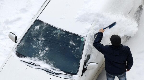 Мужчина сметает снег с машины