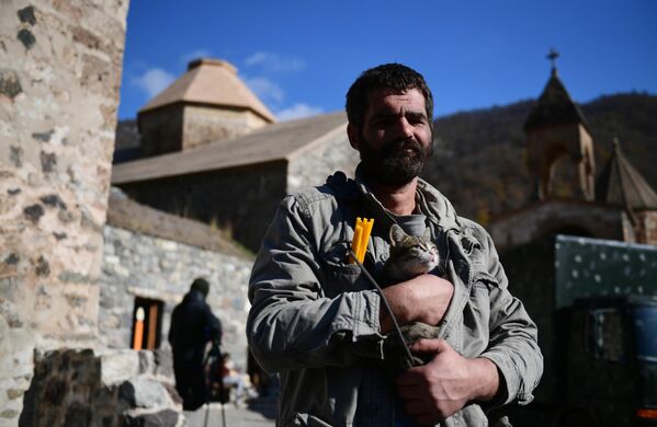 Мужчина держит на руках кота возле храма в монастыре Дадиванк в Нагорном Карабахе