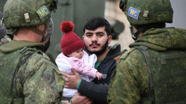 Мужчина с ребенком стоит рядом с российскими миротворцами