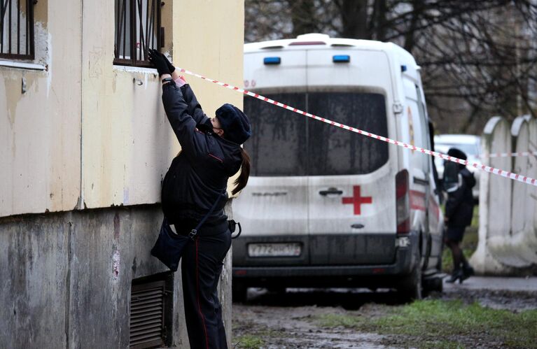 Сотрудница полиции натягивает оградительную ленту у жилого дома в городе Колпино Ленинградской области, где мужчина держит в заложниках детей в квартире