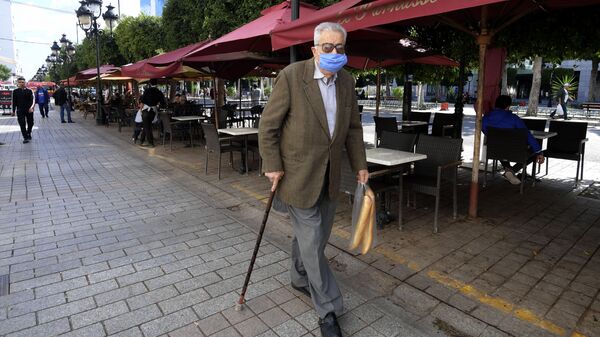 Мужчина в защитной маске проходит мимо кафе в Тунисе