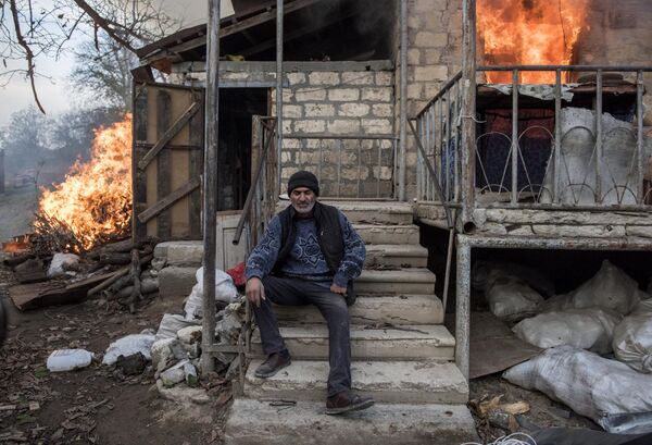 Мужчина сидит на крыльце горящего дома в поселке Карегах в Нагорном Карабахе