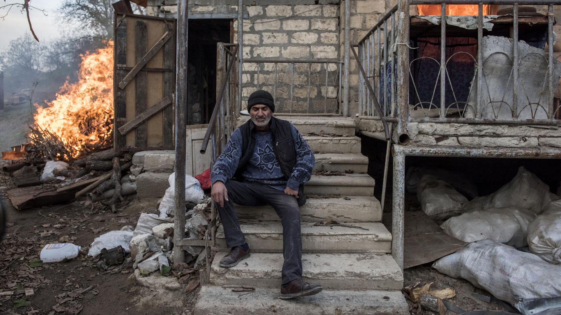 Мужчина сидит на крыльце горящего дома в поселке Карегах в Нагорном Карабахе - РИА Новости, 1920, 26.11.2020