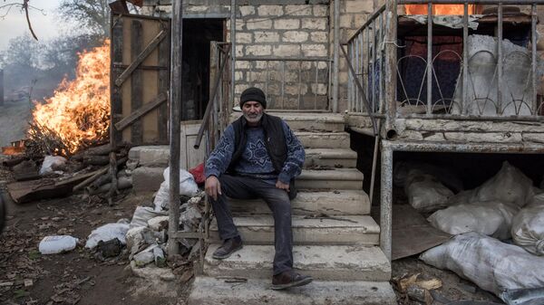 Мужчина сидит на крыльце горящего дома в поселке Карегах в Нагорном Карабахе