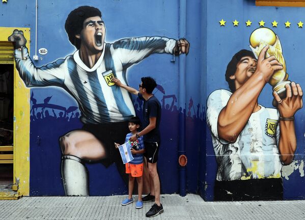 Мужчина с ребенком возле граффити с изображением аргентинского футболиста Диего Марадоны в Буэнос-Айресе