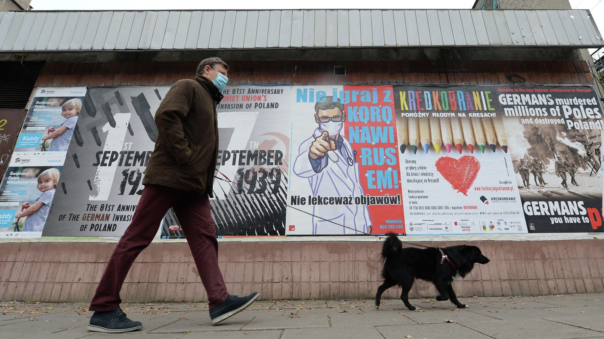 Мужчина с собакой проходит мимо плаката с предупреждением о том, что нельзя игнорировать симптомы COVID-19 в Варшаве - РИА Новости, 1920, 08.04.2021