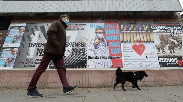 Мужчина с собакой проходит мимо плаката с предупреждением о том, что нельзя игнорировать симптомы COVID-19 в Варшаве