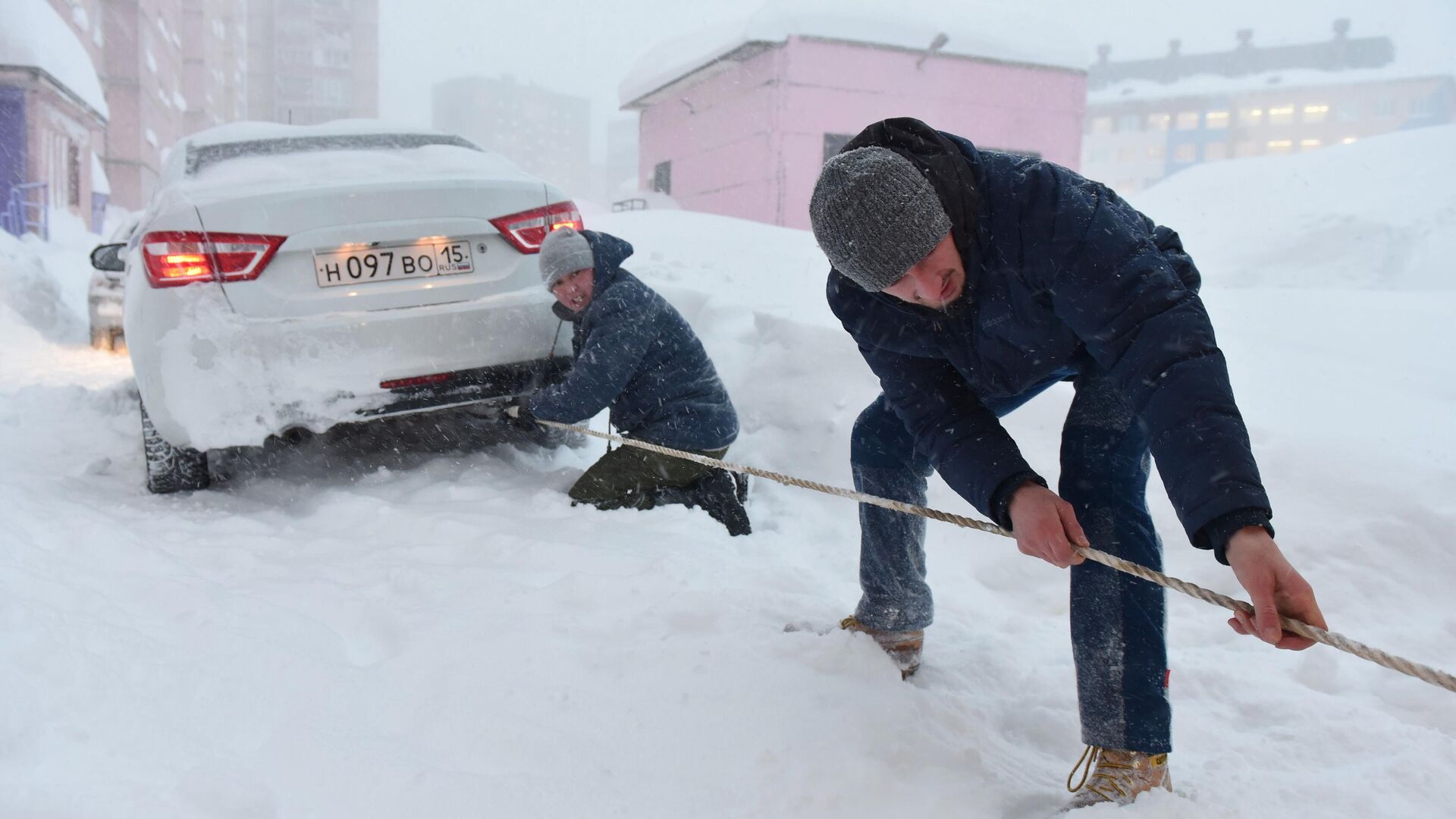 Молодые люди с помощью троса вытаскивают автомобиль, застрявший в сугробе во время снегопада в Норильске - РИА Новости, 1920, 03.12.2020