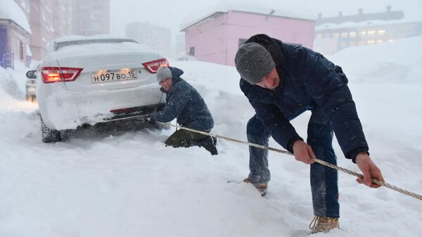 Молодые люди с помощью троса вытаскивают автомобиль, застрявший в сугробе во время снегопада в Норильске