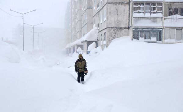 Мужчина во время снегопада на одной из улиц в Норильске