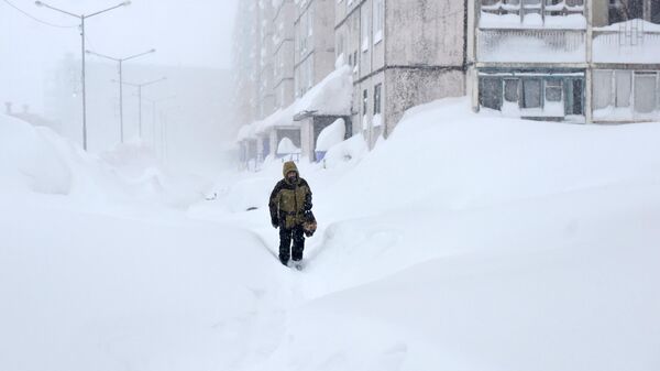 Мужчина во время снегопада на одной из улиц в Норильске