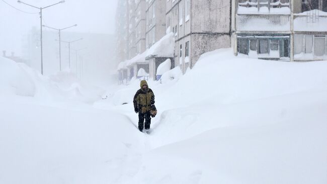 Мужчина во время снегопада на одной из улиц в Норильске