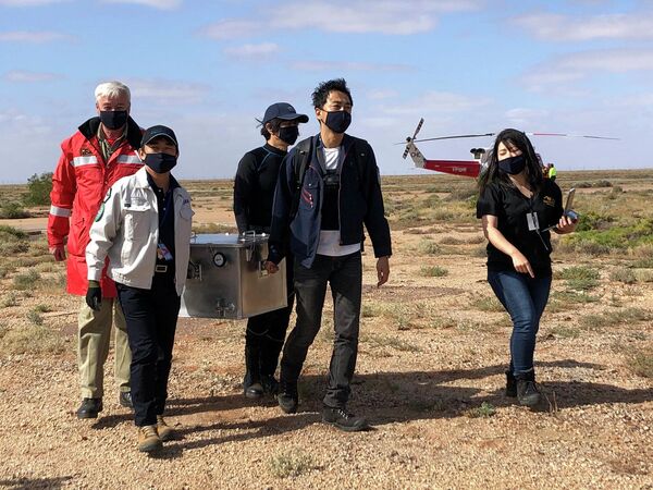 Сотрудники Японского агентства аэрокосмических исследований (JAXA) несут коробку с образцами астероида Рюгу, в районе Южной Австралии