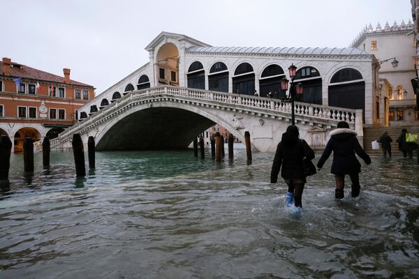 Люди проходят мимо моста Риальто во время прилива в Венеции