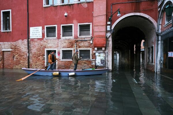 Люди катаются на традиционной лодке по затопленной улице во время прилива в Венеции