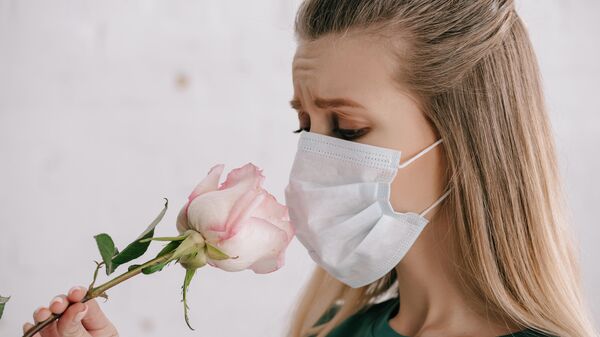 Девушка нюхает розу в медицинской маске 