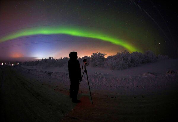 Мужчина фотографирует северное сияние на трассе Серебрянка в Мурманской области