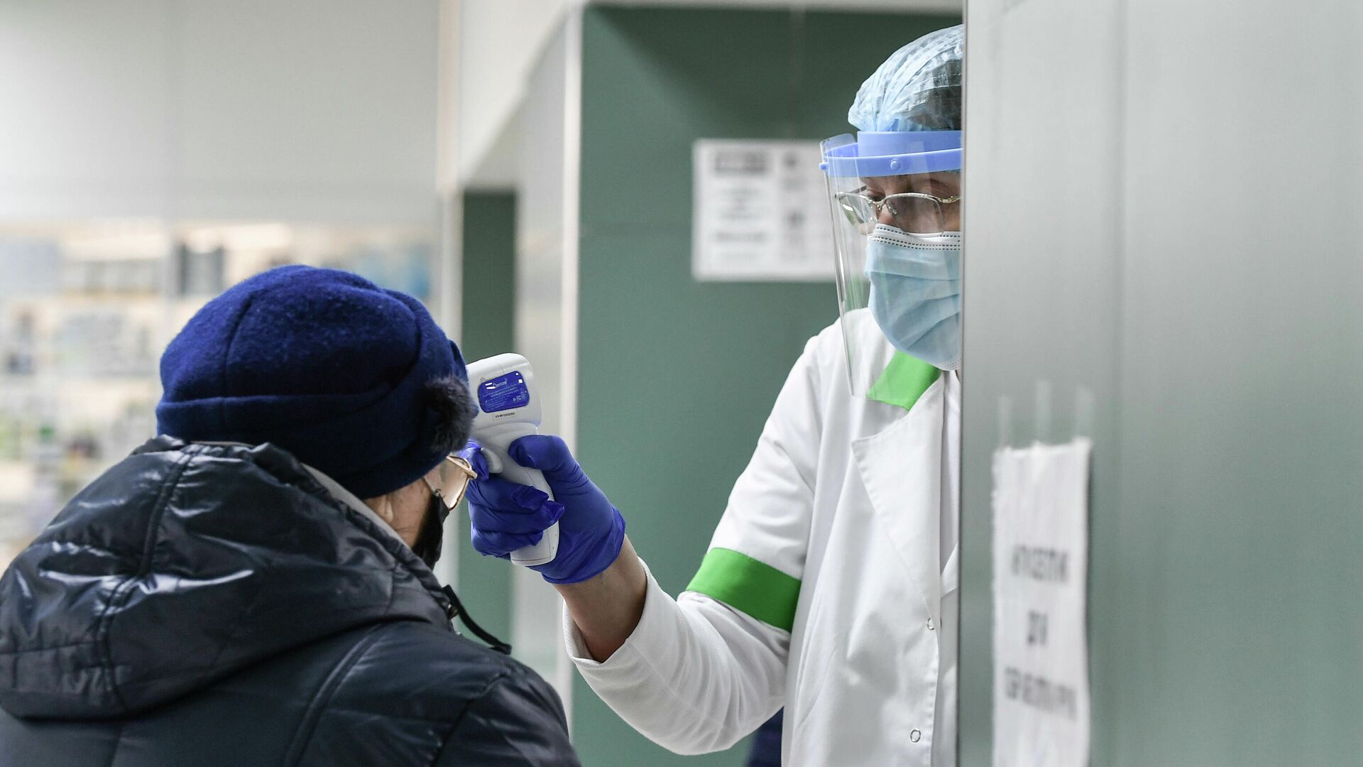 Медицинский работник проверяет температуру у пожилой женщины в защитной маске в городской поликлинике - РИА Новости, 1920, 03.02.2022