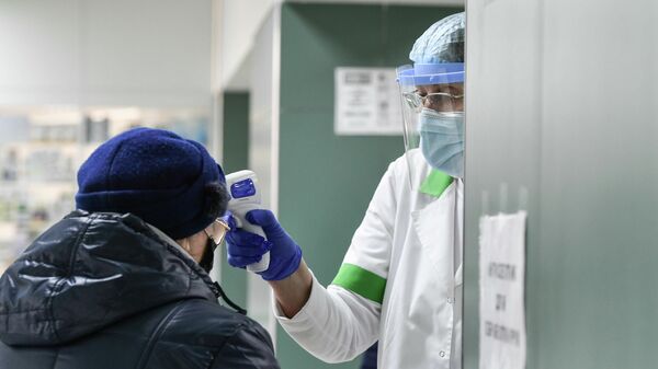 Медицинский работник проверяет температуру у пожилой женщины в защитной маске в городской поликлинике