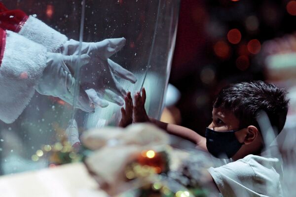 Мужчина в костюме Санта-Клауса внутри пластикового пузыря, приветствует ребенка в торговом центре в Бразилиа, Бразилия