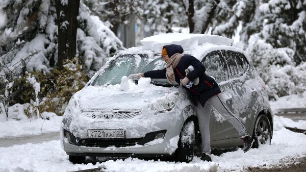 Женщина очищает свой автомобиль от снега