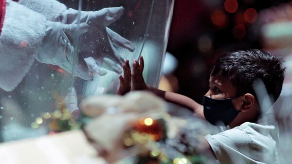 Санта-Клаус внутри пластикового пузыря приветствует ребенка в торговом центре в Бразилиа, Бразилия