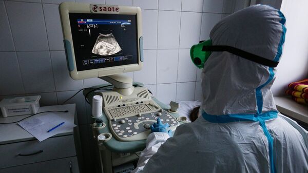Врач Новосибирской областной клинической больницы в защитном противоэпидемическом костюме проводит осмотр беременной пациентки с помощью аппарата УЗИ