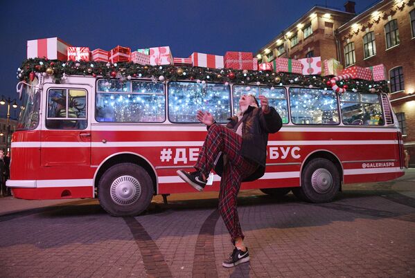 Прохожий на фоне праздничного Дедморобуса с музыкантами в костюмах Дедов Морозов, который ездит по улицам Санкт-Петербурга в преддверии нового года