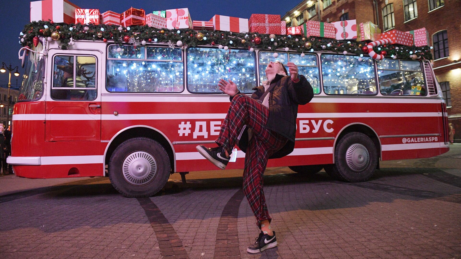 Прохожий на фоне праздничного Дедморобуса с музыкантами в костюмах Дедов Морозов, который ездит по улицам Санкт-Петербурга в преддверии нового года - РИА Новости, 1920, 31.12.2020