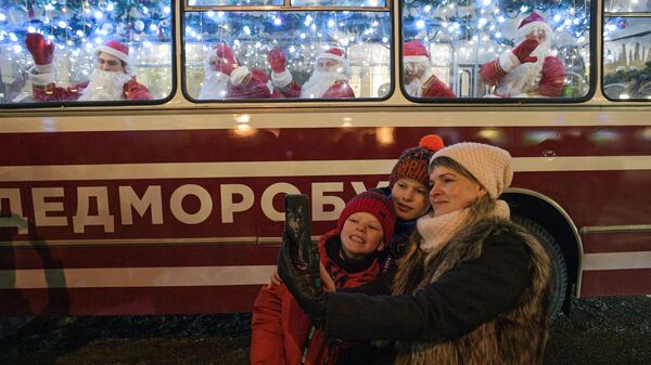 Прохожие фотографируются на фоне праздничного Дедморобуса с музыкантами в костюмах Дедов Морозов, который ездит по улицам Санкт-Петербурга в преддверии нового года
