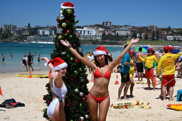 Девушки фотографируются у рождественской ели, установленной на пляже в Сиднее, Австралия