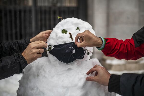Люди надевают маску на слепленного снеговика на одной из улиц в Мадриде