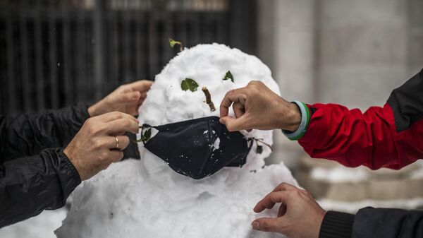 Люди надевают маску на слепленного снеговика на одной из улиц в Мадриде
