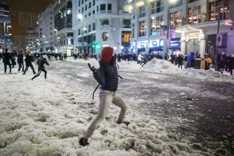 Юноша бросает снежок во время игры в снежки на площади Кальяо в Мадриде