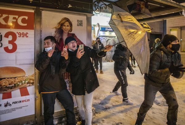 Юноши прячутся за зонтом во время игры в снежки на площади Кальяо в Мадриде