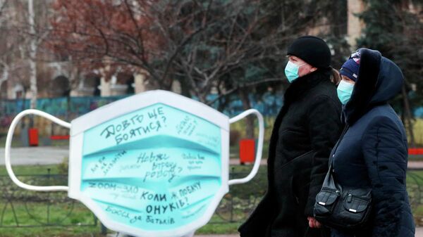 Женщины проходят мимо инсталляции в виде защитной маски на улице в Киеве