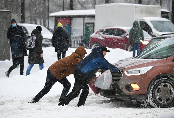 Мужчины толкают машину, застрявшую на дороге во время снегопада